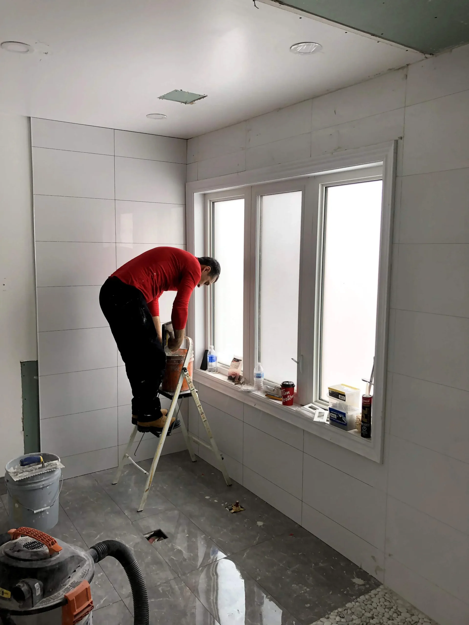 Refined Renos team member working on a bathroom with tiled walls and unfinished ceiling